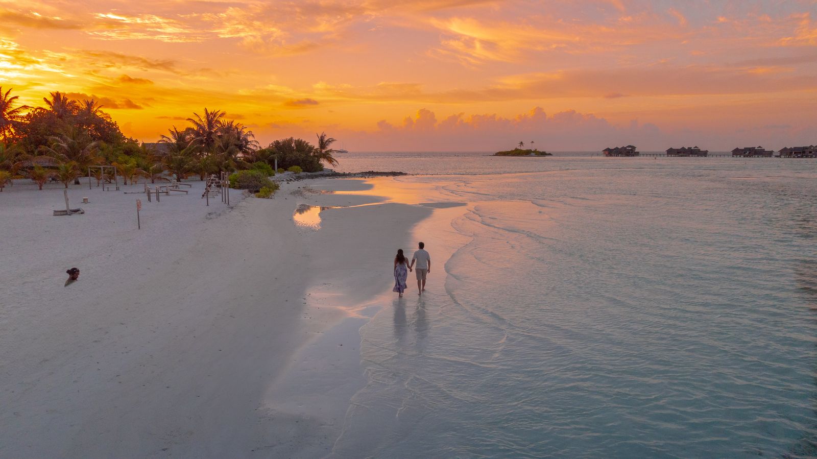 Couple strolling on a tropical beach at sunset, seen from above