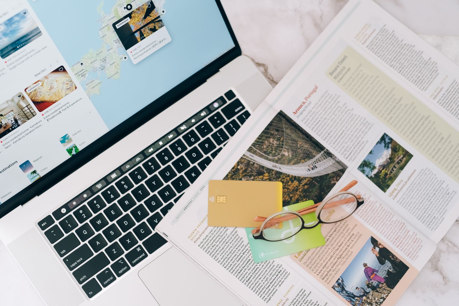Open laptop next to a travel magazine and a pair of glasses